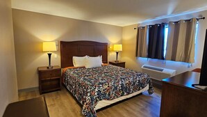 A hotel room with a bed, two bedside tables with lamps, a flat-screen TV, a window with curtains, and an air conditioning unit. - Farwest Motel (Everett)