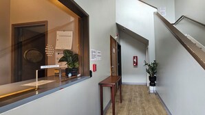 A hotel reception area with a desk, a plant, a fire extinguisher, a staircase, and a door. - Farwest Motel (Everett)