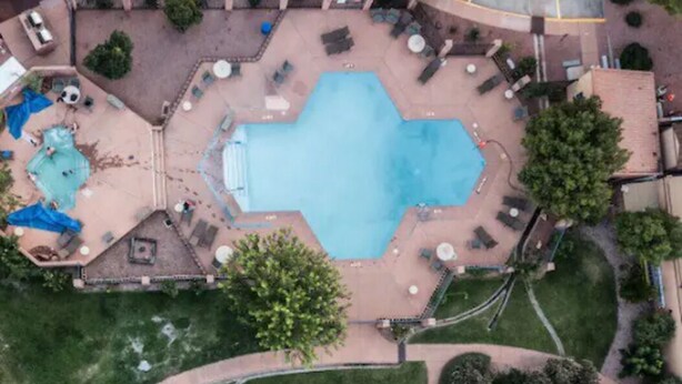Vue aérienne d’un espace piscine avec une piscine rectangulaire, entourée de chaises longues et d’une petite terrasse.