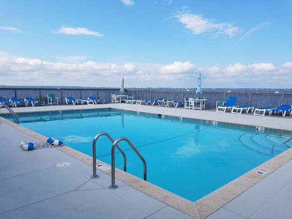 A swimming pool with blue water, surrounded by lounge chairs and a deck.