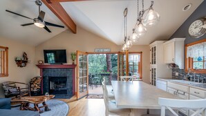 A spacious living area with a fireplace, a dining table, and a kitchen with white cabinets. - Cozy cabin with Hot tub Fireplace Fire pit Full kitchen Close to town and RMNP. (Estes Park)