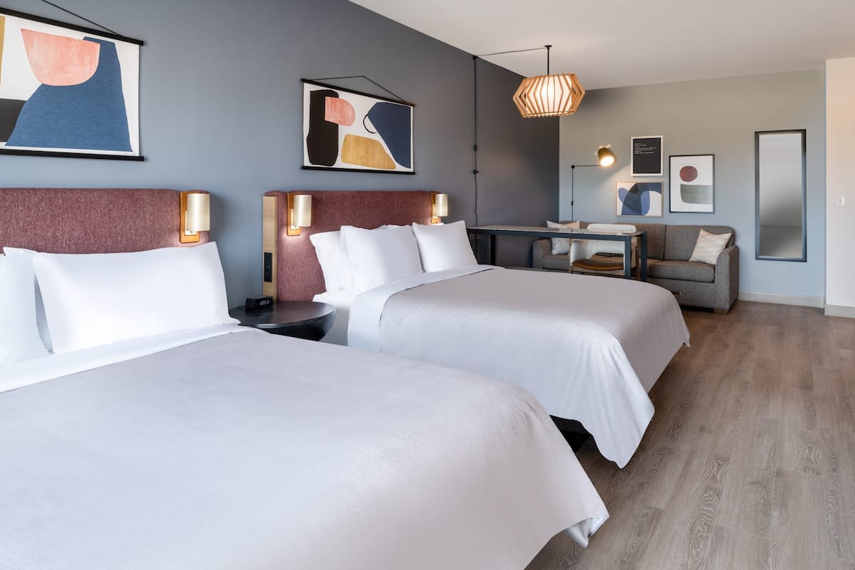 Een hotelkamer met twee bedden, een bureau, een bank en kunstwerken aan de wanden.