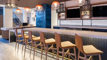 A modern kitchen with a bar area, bar stools, pendant lighting, and a staircase in the background.