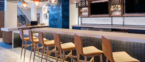 A modern kitchen with a bar area, bar stools, pendant lighting, and a staircase in the background.
