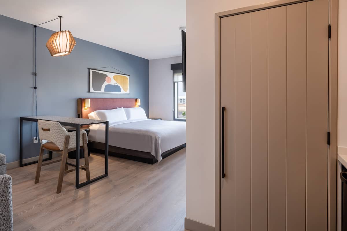 Een moderne hotelkamer met een bed, bureau, stoel en kledingkast.
