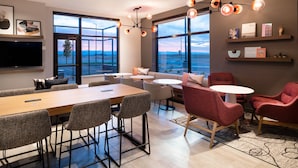 A modern hotel room with a large wooden table, comfortable seating, a flat-screen TV, and large windows offering a view of the desert landscape.