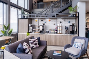 A modern living space with a sofa, armchair, and coffee table. A kitchen area with appliances and a staircase is visible in the background.