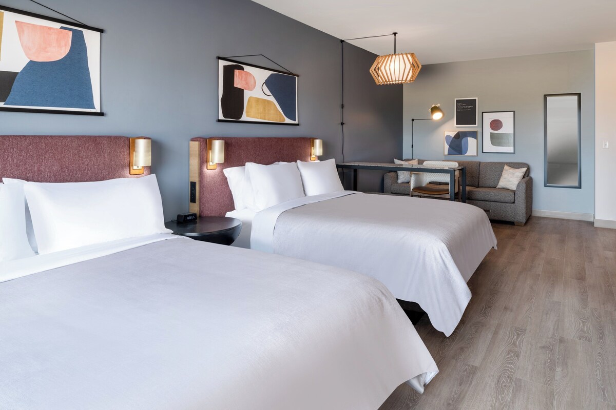 Een hotelkamer met twee bedden, een bureau, een bank en kunstwerken aan de wanden.