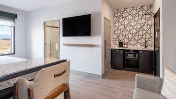 A modern kitchen with a flat-screen TV, wooden cabinets, and a microwave.