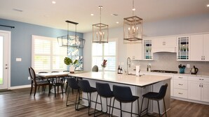 A modern kitchen with a large island, bar stools, and pendant lighting.