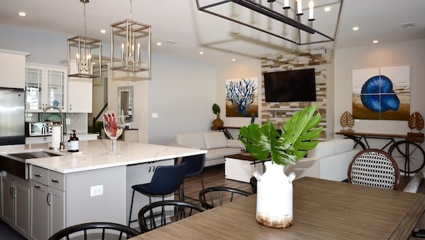 A modern kitchen with a central island, pendant lighting, and a dining area with a wooden table and chairs.