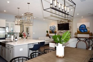 A modern kitchen with a central island, pendant lighting, and a dining area with a wooden table and chairs. - Stunning Home Pet Friendly Resort Style Amenities Quick Ride to Beach (Ocean View)