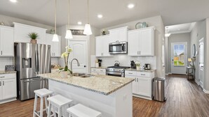 A modern kitchen with white cabinetry, stainless steel appliances, and a central island with bar stools. - New Modern Home, Lakefront, Park & Pool, spacious 4br/3ba very safe place<br> (Baton Rouge)