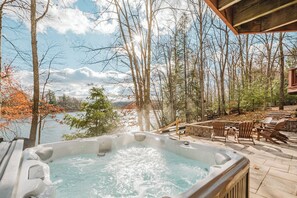 A hot tub with a view of a lake and trees, surrounded by outdoor furniture and a stone patio. - Eagle's Landing by Taylor Made Deep Creek (McHenry)