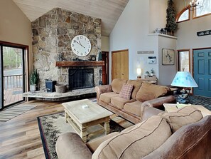 A cozy living room with a stone fireplace, a large clock, and a comfortable seating area. - Eagle's Landing by Taylor Made Deep Creek (McHenry)