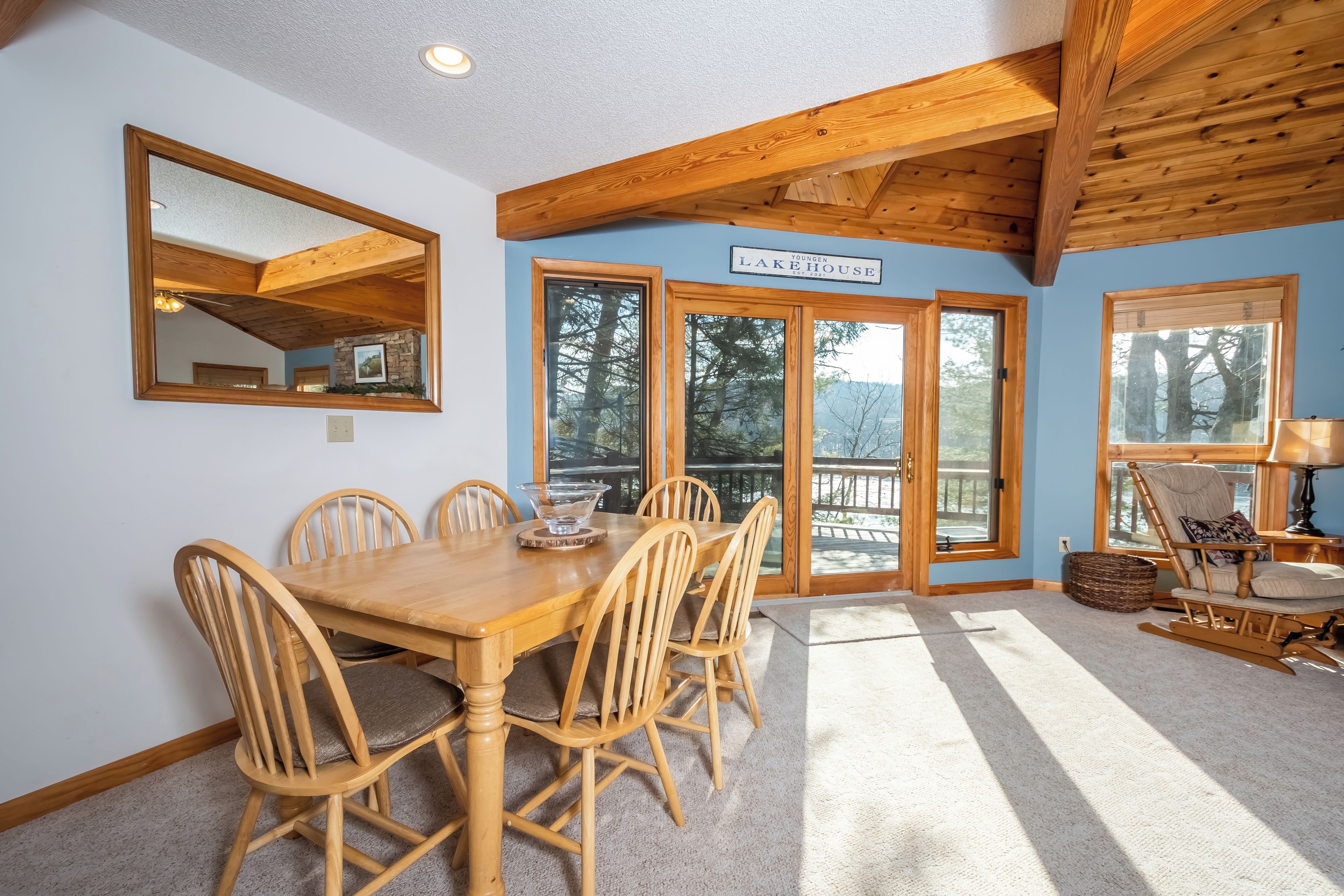 A dining area with a wooden table and chairs, a large mirror, and a sign reading 'Lakeside Lodge.'