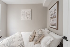 Une chambre à coucher bien rangée, avec un lit, des oreillers et deux œuvres d’art accrochées au mur.