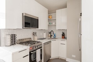 Une cuisine moderne avec des meubles blancs, un four à micro-ondes encastré, une cuisinière à gaz et un lave-vaisselle.