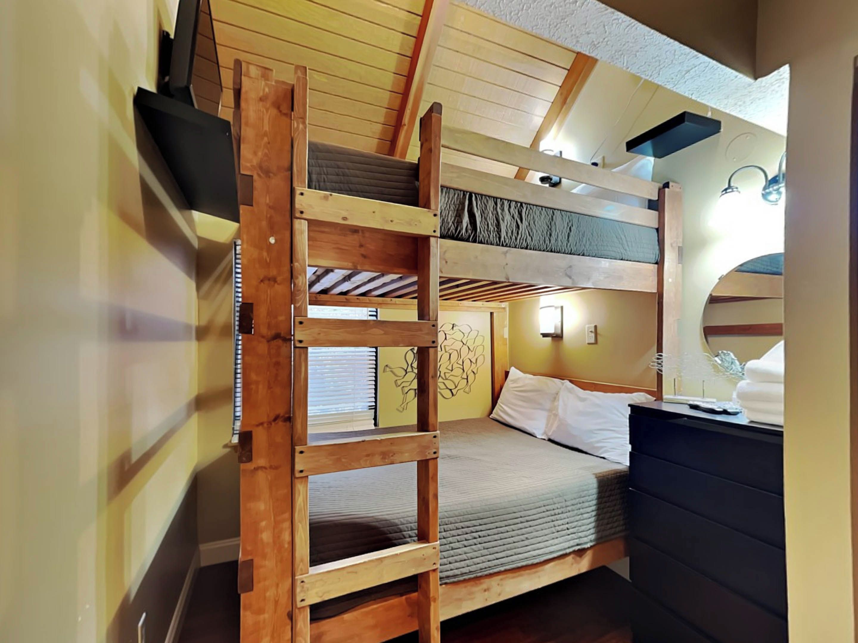 A compact bedroom with a bunk bed, a small desk, and a mirror.