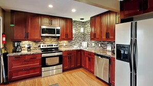 A modern kitchen with wooden cabinets, stainless steel appliances, and a granite countertop. - Loft of Luxury by Taylor Made Deep Creek (Oakland)