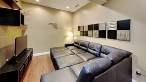 A modern living room with a sectional sofa, a flat-screen TV, and a wall-mounted art piece. - Loft of Luxury by Taylor Made Deep Creek (Oakland)
