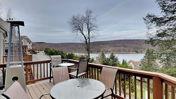 A deck with a glass table and chairs, overlooking a lake and hills. - Loft of Luxury by Taylor Made Deep Creek (Oakland)