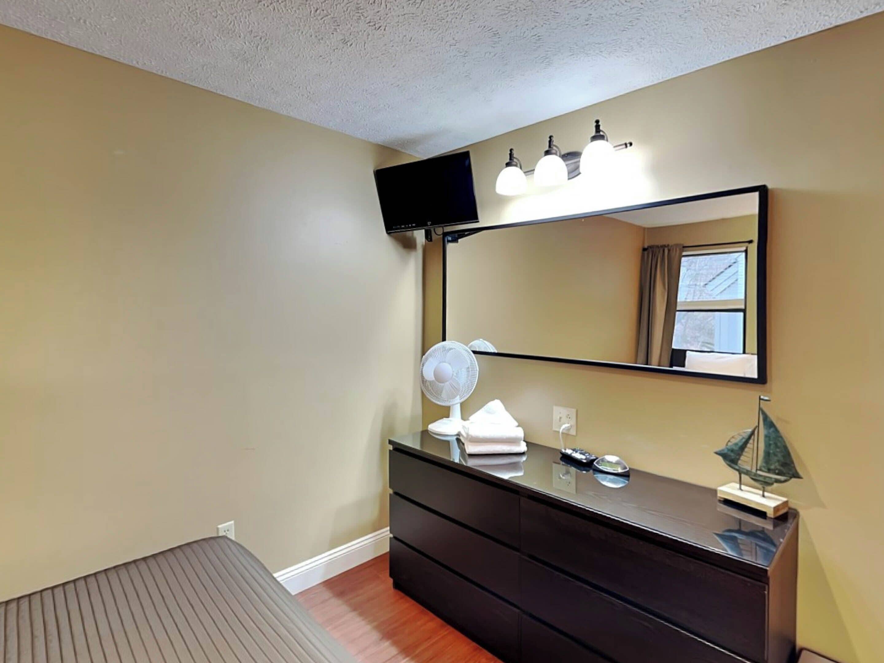 Een slaapkamer met een bed, een dressoir, een spiegel, een televisie en een raam met gordijnen.