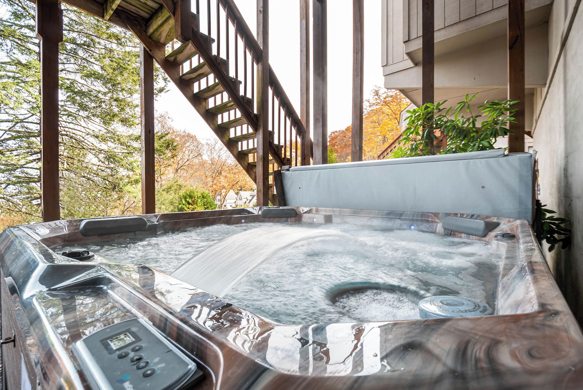 Un jacuzzi con panel de control, rodeado de vigas de madera y vistas a árboles otoñales.