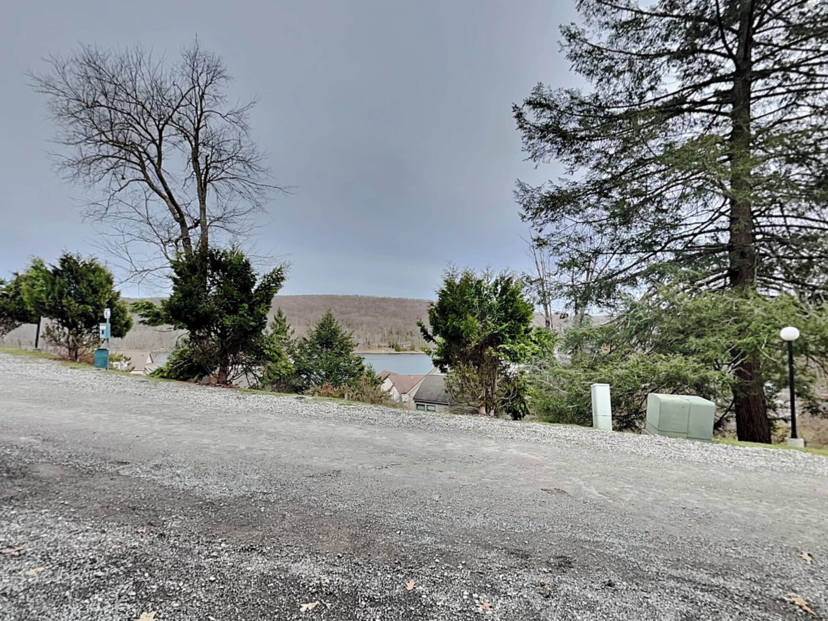 Un camino de grava que conduce a una casa con vistas a un lago y árboles.