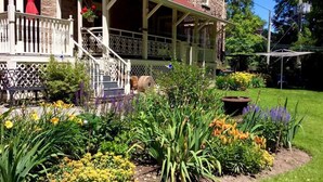 A house with a covered porch, steps leading to the entrance, and a garden with various plants and flowers.