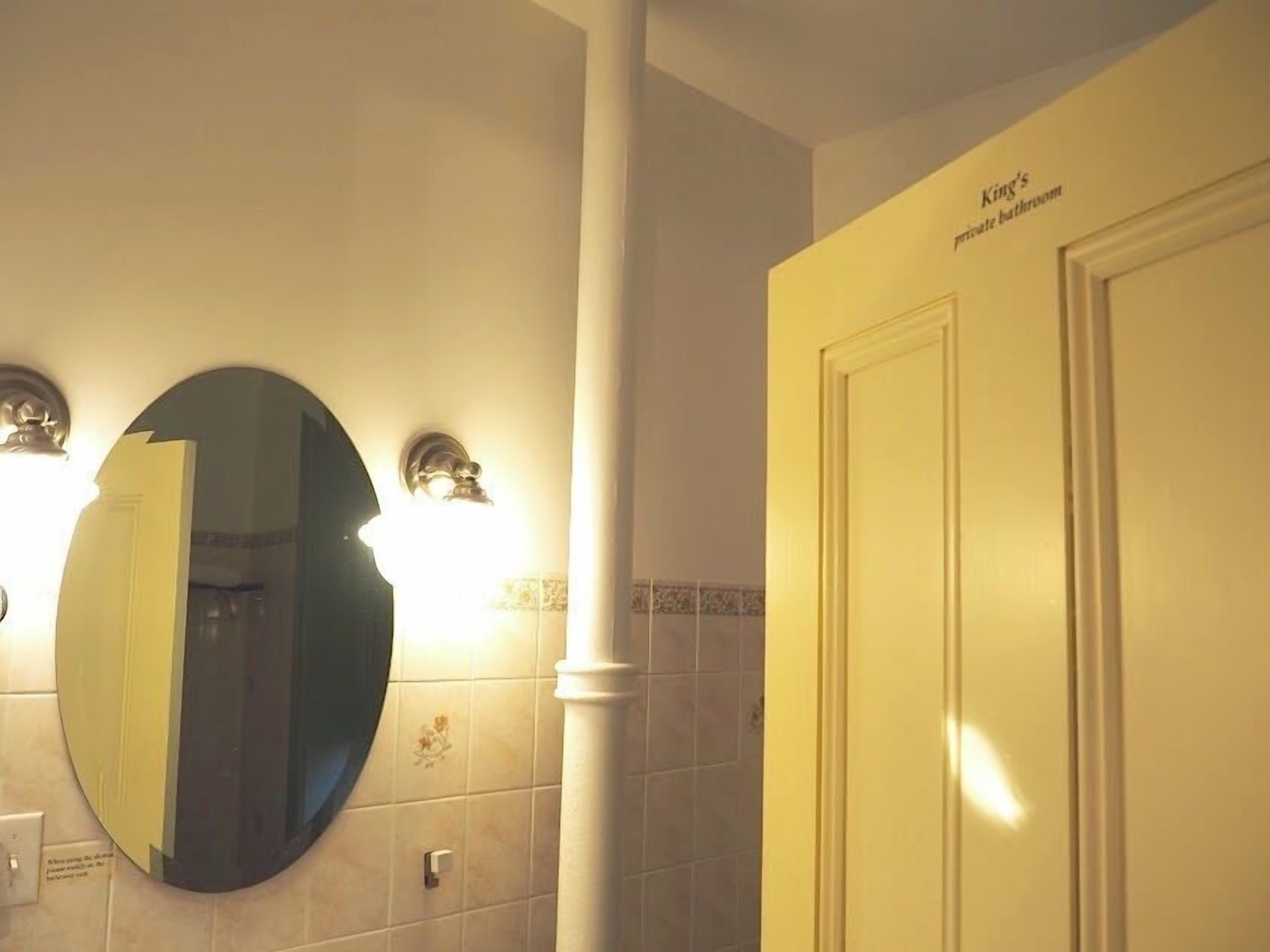 A private bathroom with a large mirror, wall-mounted lights, and a door labeled "King's private bathroom".