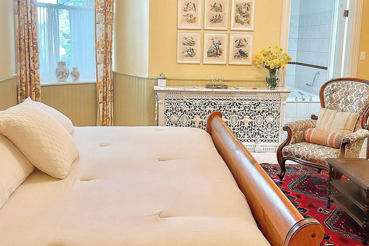 Un dormitorio espacioso con una cama grande, un cabecero de madera, una araña, una mesa de comedor con sillas y obras de arte en la pared.