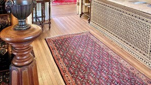 A traditional interior with a wooden floor, a patterned rug, a decorative urn, a table lamp, and a cabinet with intricate carvings.