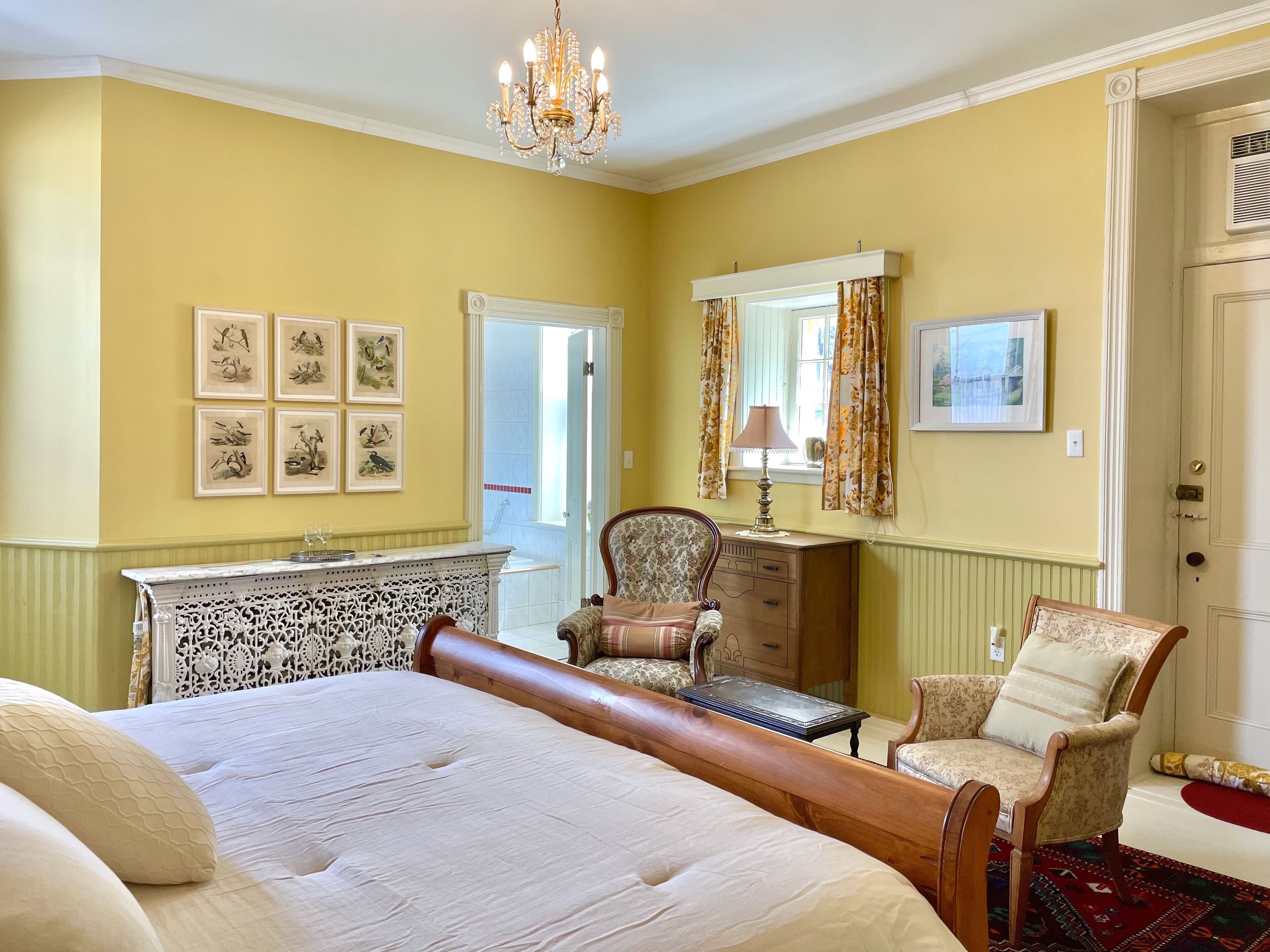 A bedroom with a large bed, a wooden headboard, a chair, a dresser, and a chandelier.