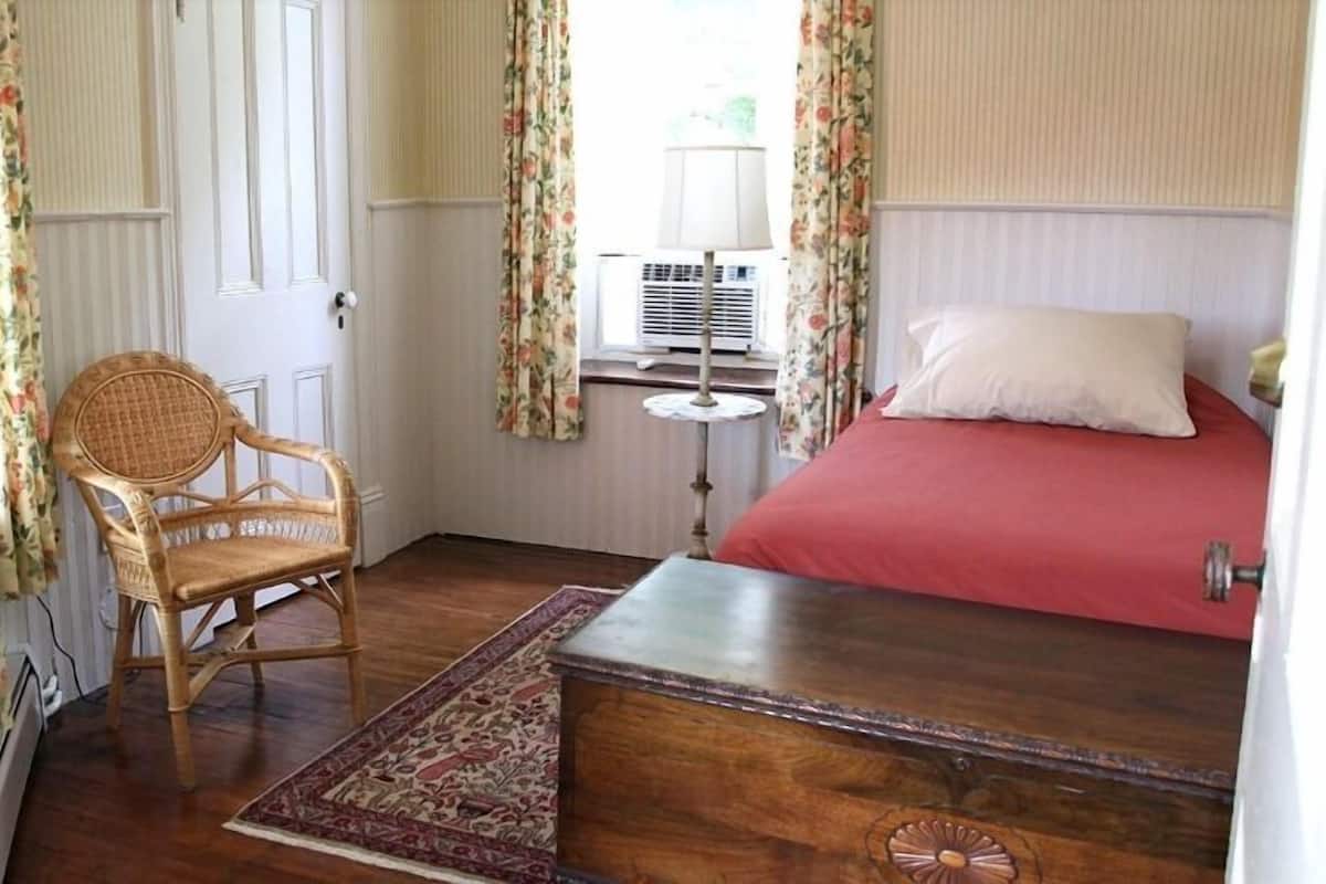 Un dormitorio con una cama de madera, una silla de mimbre, una mesita pequeña y un tapete estampado.