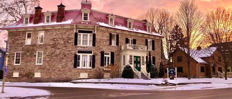 A stone building with a red roof, a front porch, and a snow-covered landscape.