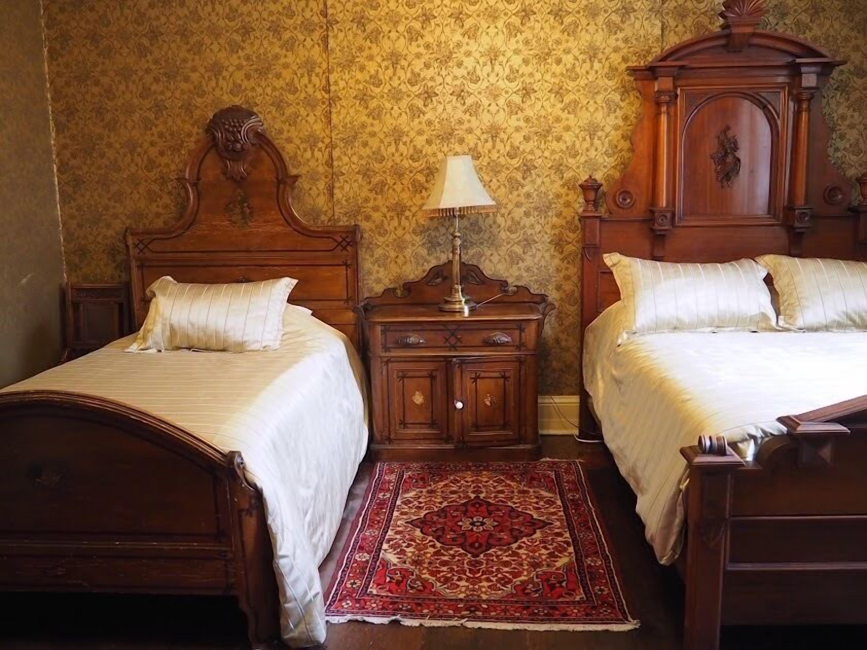 Un dormitorio tradicional con dos camas de madera, una mesita de noche y un tapete rojo estampado.