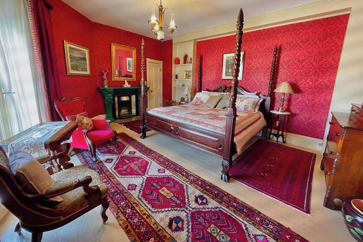 Un dormitorio tradicional con cama con dosel, alfombra roja y chimenea.