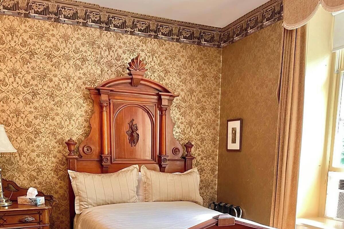 Un dormitorio tradicional con una cama de madera, una mesita de noche, una lámpara y una ventana con cortinas.