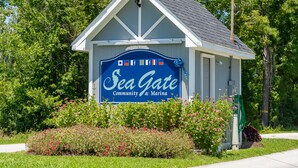 Un petit bâtiment sur lequel on peut lire l’inscription « Sea Gate Community & Marina », entouré de verdure et de fleurs.
