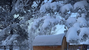 Een houten gebouw bedekt met sneeuw, met een schuin dak, omgeven door sneeuwbezwaarde bomen.