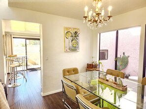 A dining area with a glass table and chairs, a chandelier, and a painting on the wall. - Rancho Mirage/PD border 
28 day min 
3bed, 2bath Pools, tennis/pickleball gated! (Palm Desert)