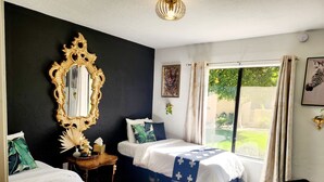 Een slaapkamer met twee bedden, een grote, versierde spiegel, een tafeltje met een lamp, en uitzicht op groen buiten.