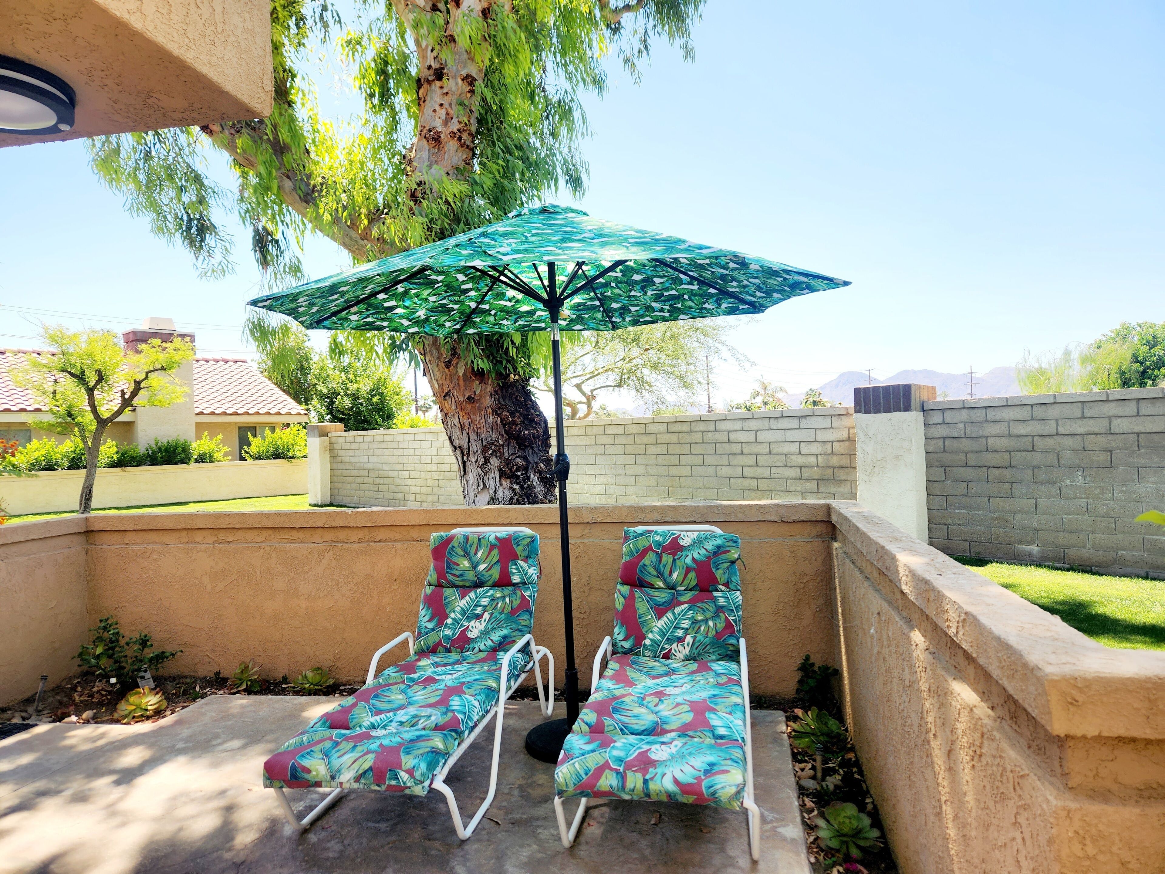 Une terrasse extérieure avec deux chaises longues et un parasol vert.
