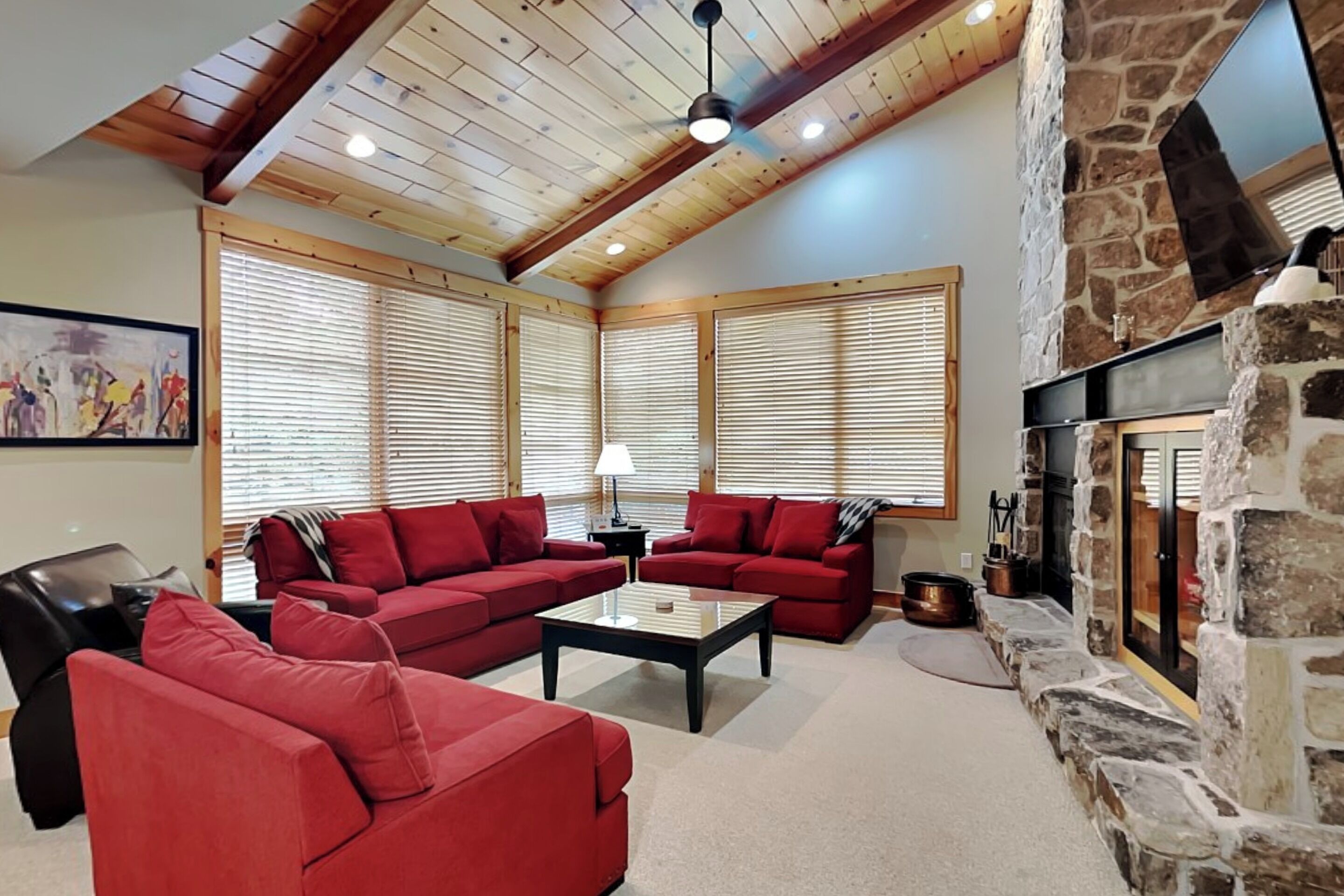 A living room with red sofas, a coffee table, a stone fireplace, and wooden ceiling beams.