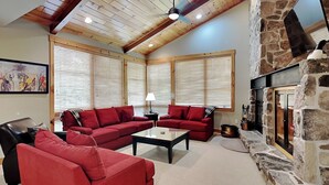 A living room with red sofas, a coffee table, a stone fireplace, and wooden ceiling beams. - Retreat on Main Street by Taylor Made Deep Creek (McHenry)