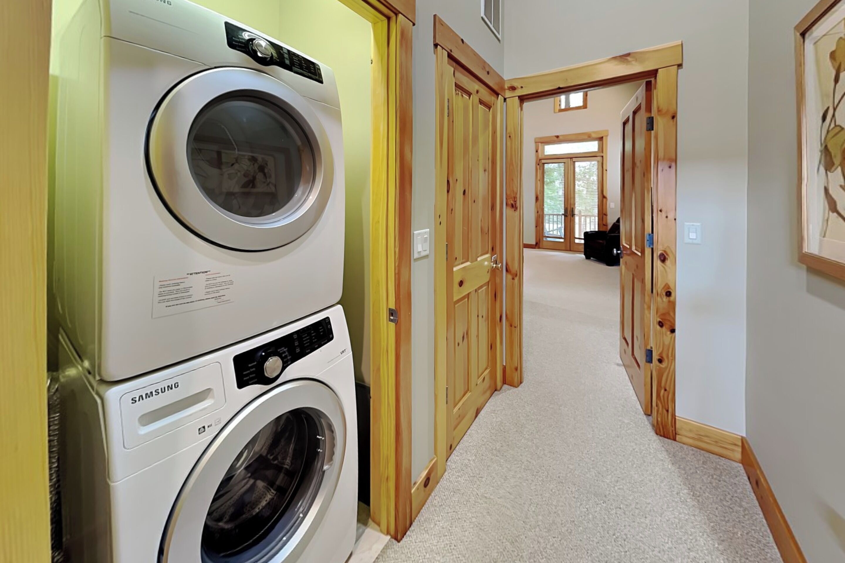 A laundry area with stacked washing machines, a hallway with wooden doors, and a carpeted floor.