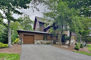 A modern two-story house with a stone foundation, a wooden garage door, and a driveway. - Retreat on Main Street by Taylor Made Deep Creek (McHenry)