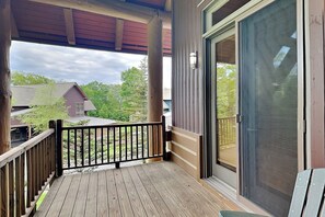 A wooden deck with a black railing, a sliding glass door, and a view of neighboring houses. - Retreat on Main Street by Taylor Made Deep Creek (McHenry)