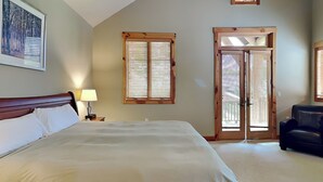 A bedroom with a large bed, a nightstand with a lamp, a wooden door, and a framed picture on the wall. - Retreat on Main Street by Taylor Made Deep Creek (McHenry)